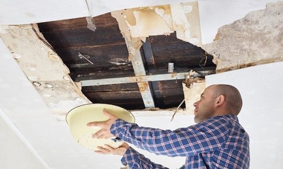Man catching water with bucket from damaged ceiling
