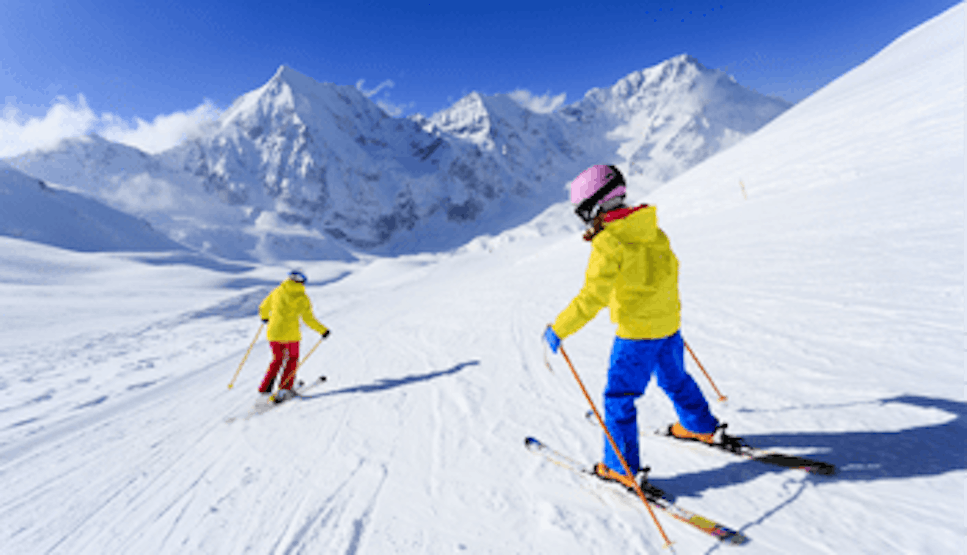 Two people in yellow jackets skiing down a mountain