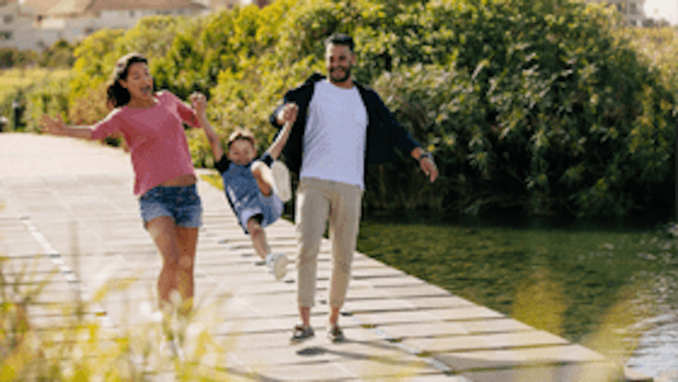 Man and women playfully swinging a child near a lake