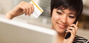 Woman talking on the phone holding a credit card and smiling