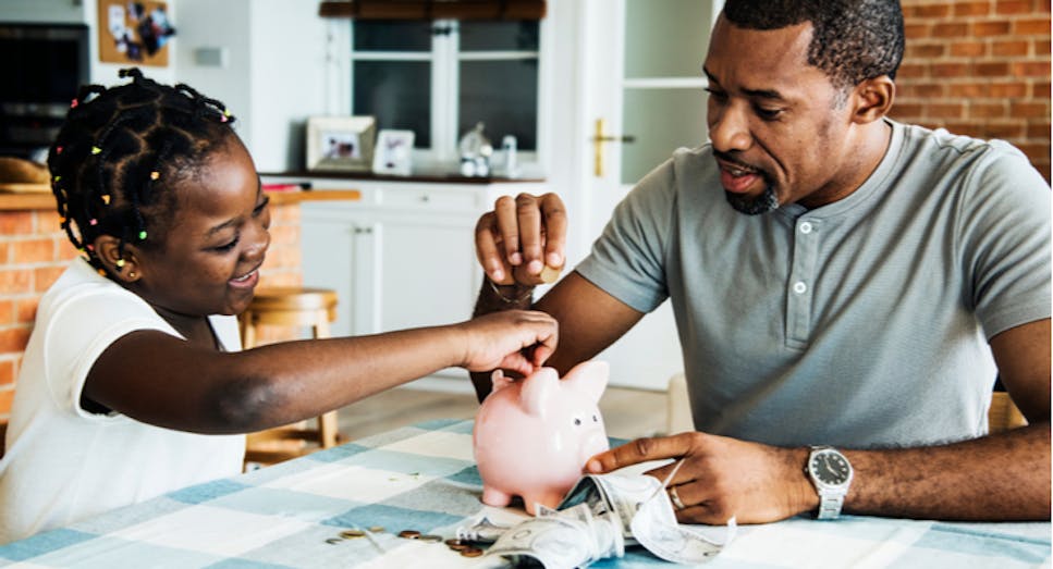 Child with dad putting money into piggy bank