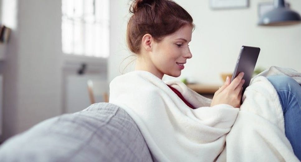 Woman using tablet on sofa in blanket