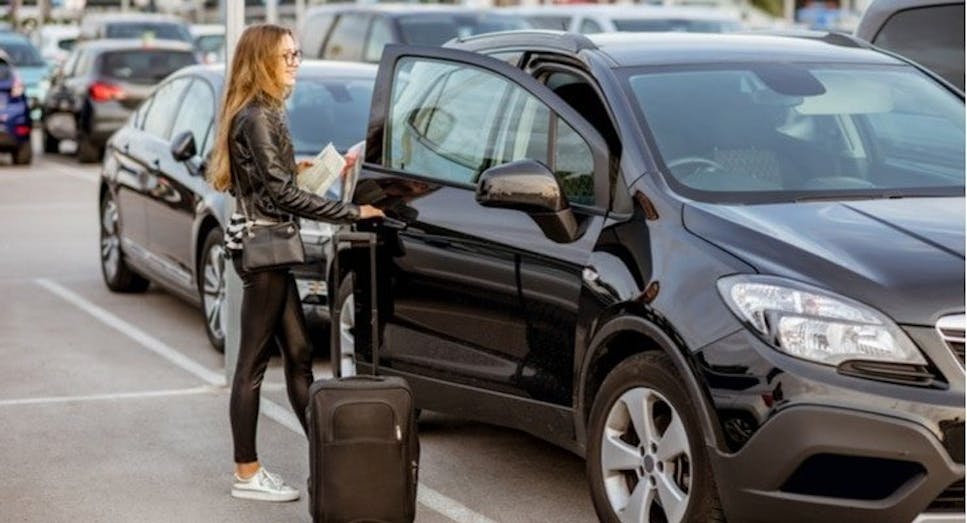 Female traveller with suitcase getting into a black car