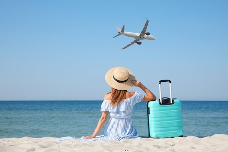 Woman on beach watch a plane with suitcase