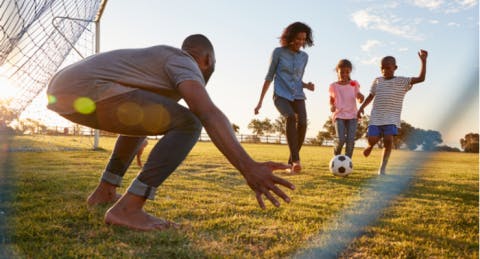 family playing football outdoors in a park 
