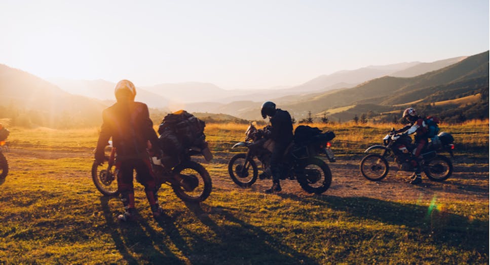 Photo of several motorcyclists in a field viewing the sunset