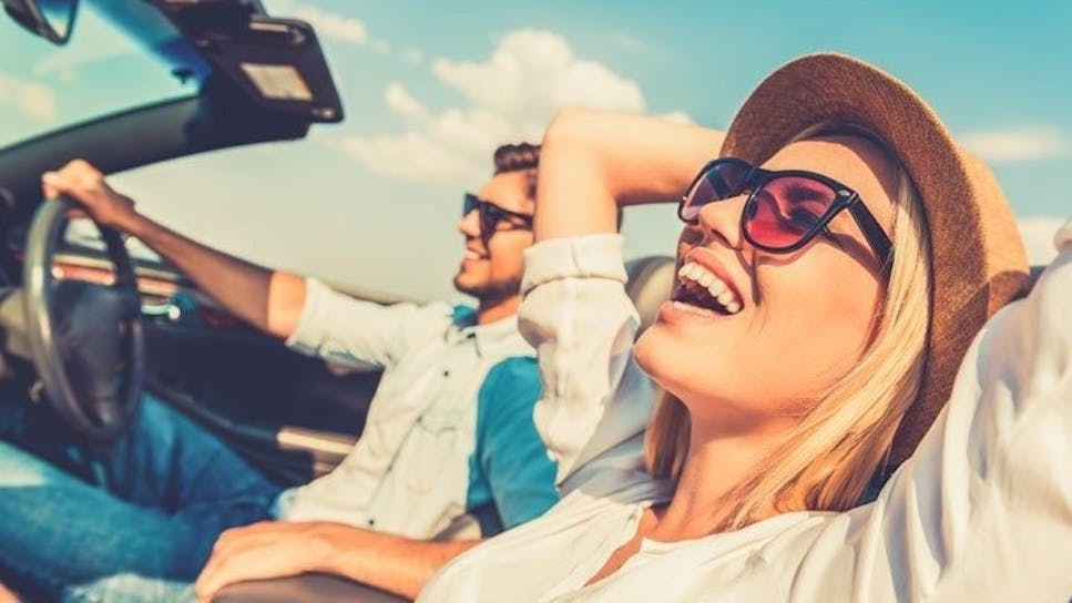 woman in sunglasses relaxing in passenger seat of car next to male driver 