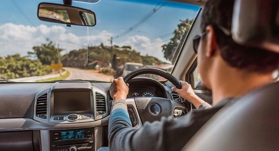 Person driving car on road in summer