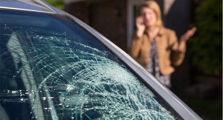 Woman on phone next to broken car windscreen