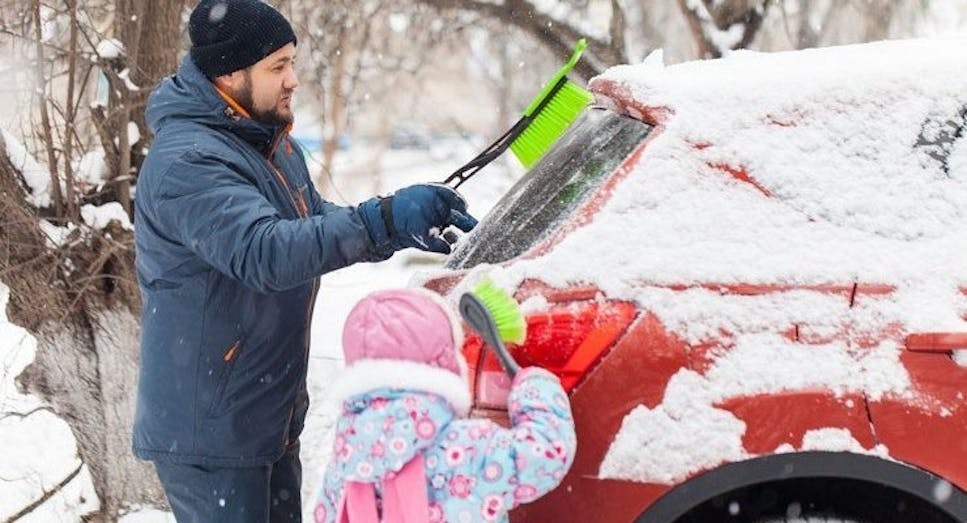 Man and daughter brushing snow off car