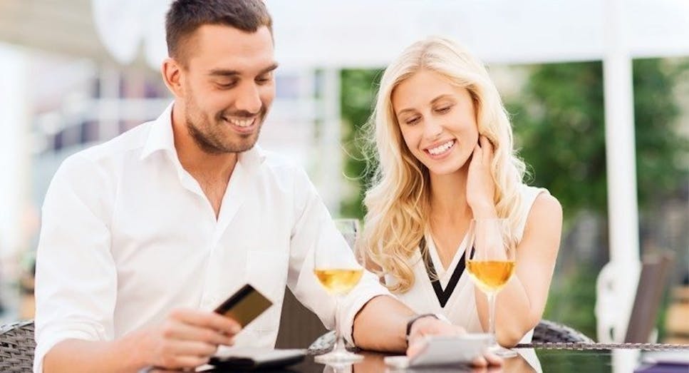 Couple on holiday paying for meal at an al fresco restaurant