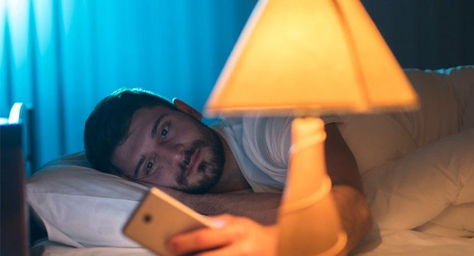 Man turning on lamp from bed