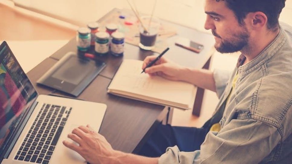 man working at home using laptop and making notes