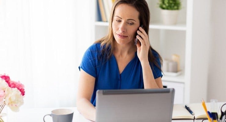Woman on phone sat in front of laptop