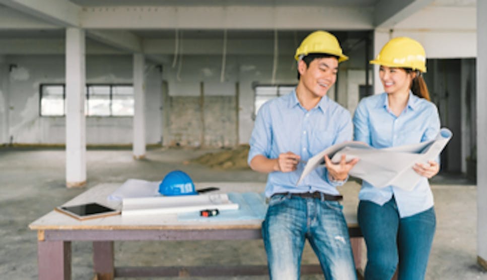 A smiling woman and man looking at plans on work site, in hardhats