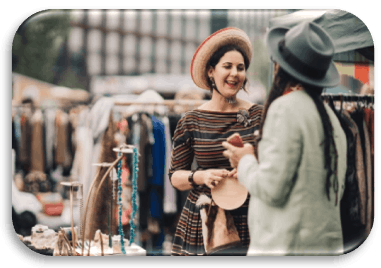 Image showing a buyer and seller talking at a car boot sale. The buyer has tried on a hat.