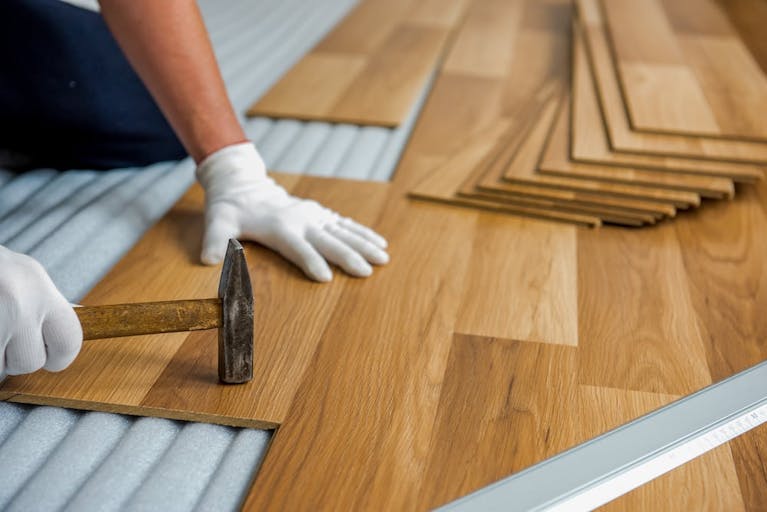 White gloved hands holding a hammer and putting laminate flooring in place