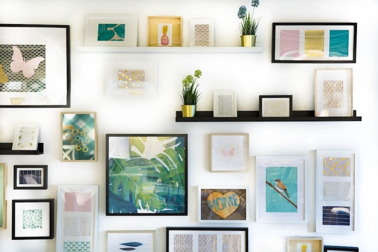 A white wall covered in framed pictures, with black, white and brown frames