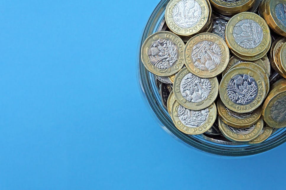 A jar of pound coins against a blue background.