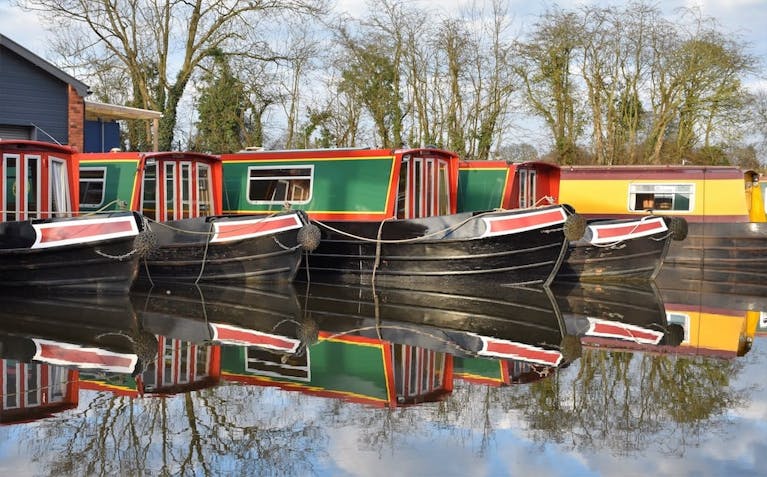Colourful canal boats moored side by side, reflected in the water