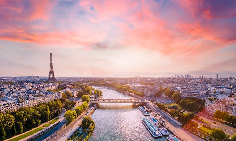 A Paris landscape, including the river and, in the distance, the Eiffel Tower. The sky is blue and pink.