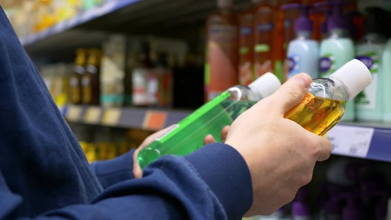 Hands holding toiletries next to supermarket shelves.