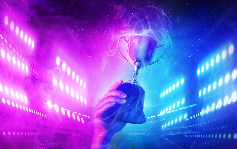 A Caucasian hand holding a generic silver trophy against a background of blue and pink neon lights
