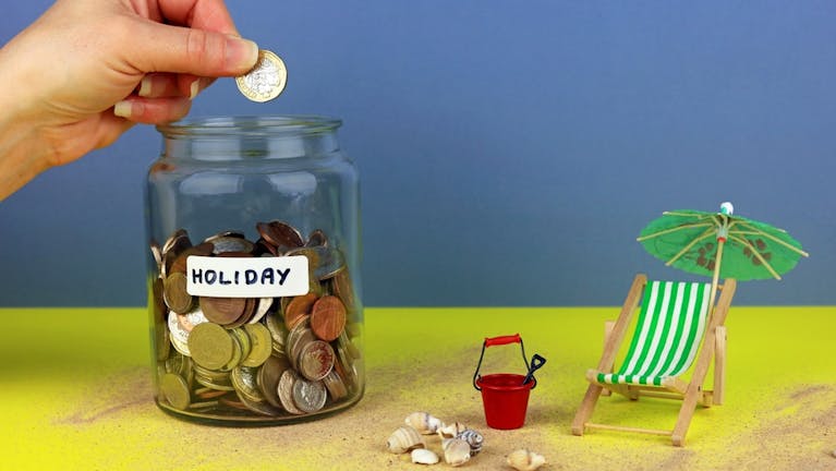 A jar of coins labelled 'holiday' and a tiny model deckchair and bucket