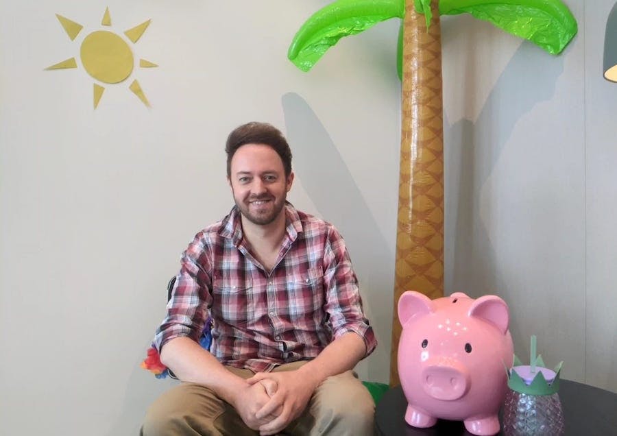 MSE Oli sits smiling beside an inflatable palm tree and a giant piggy bank.