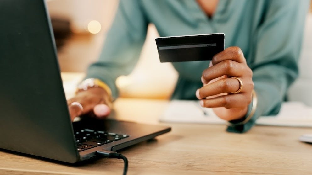 Woman holding her debit card with one hand and using a laptop with another
