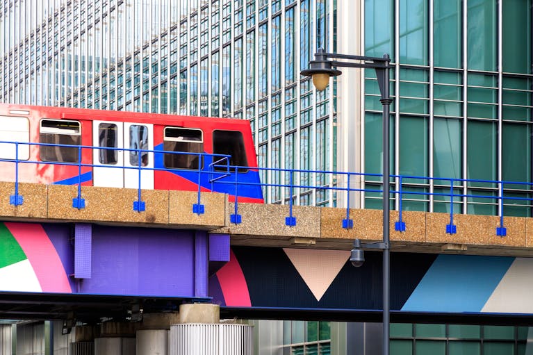 Bright red DLR train passing over colourful bridge among Canary Wharf skyscrapers