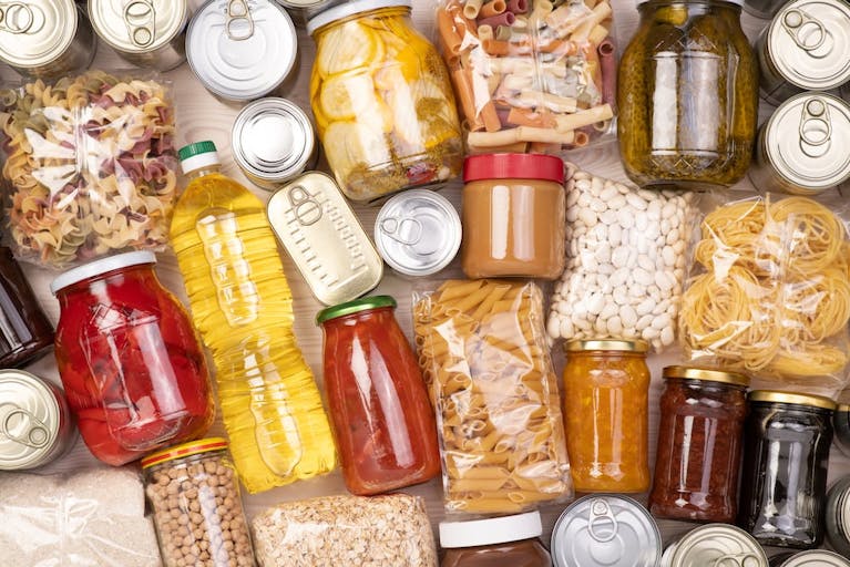 Lots of food items laid on their sides, including packets of pasta, cans and jars of preserves