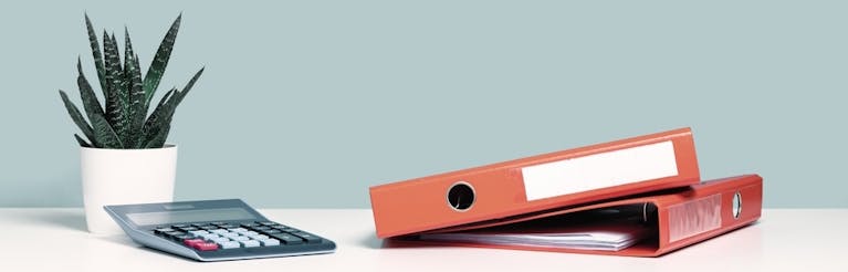 Calculator and red document binders on a white desk alongside potted cactus