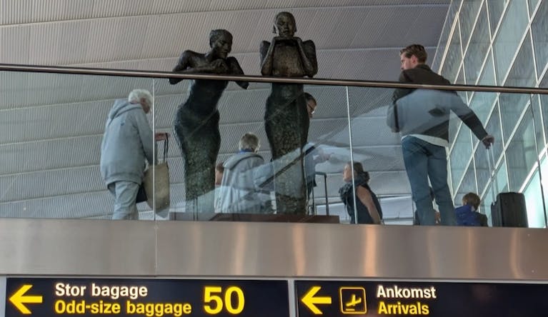 Two statues of women appear to look down from an upper floor at Copenhagen airport, above the information boards