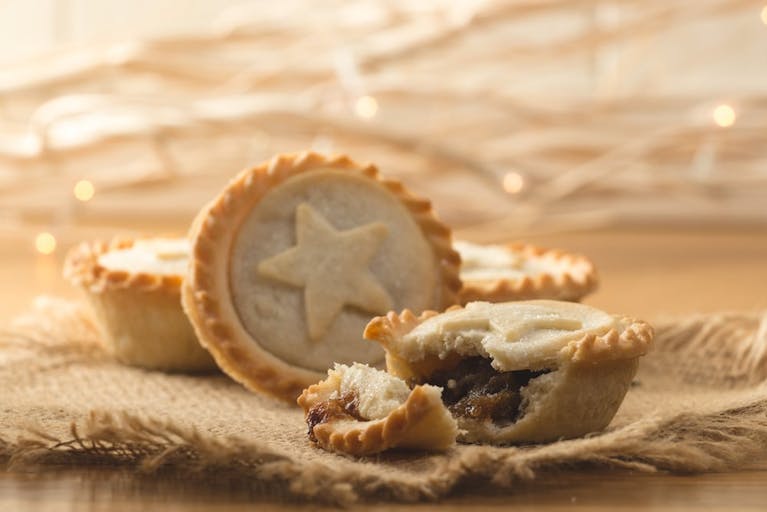 Mince pies on a piece of brown cloth. One mince pie has had a bite taken out of it.