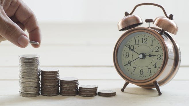 A hand putting coins into piles on a table next to an alarm clock