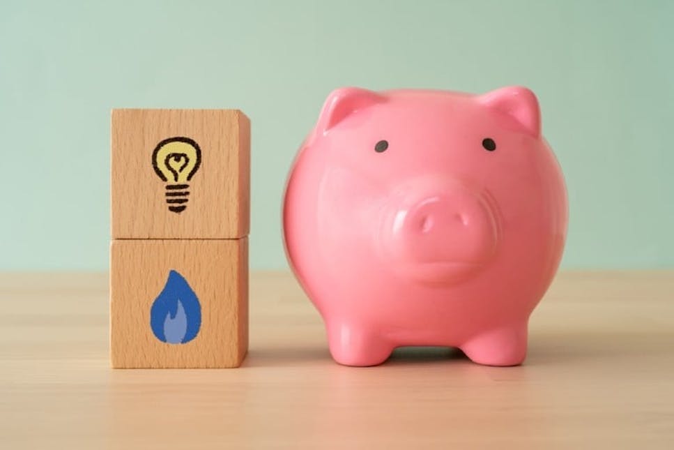 Piggy bank on table next to blocks with electricity and water signs on them
