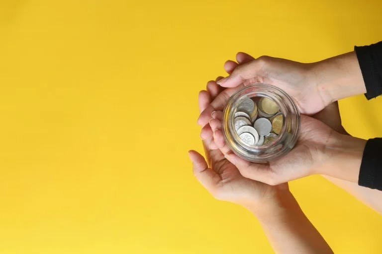 Two people holding a jar of coins against a yellow background.