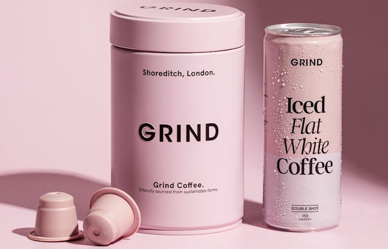 An image of a Grind coffee tin, two coffee pods, and a can of Grind iced flat white coffee