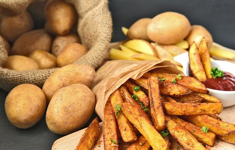 A sack of potatoes, some chips wrapped in brown paper and a ramekin of ketchup