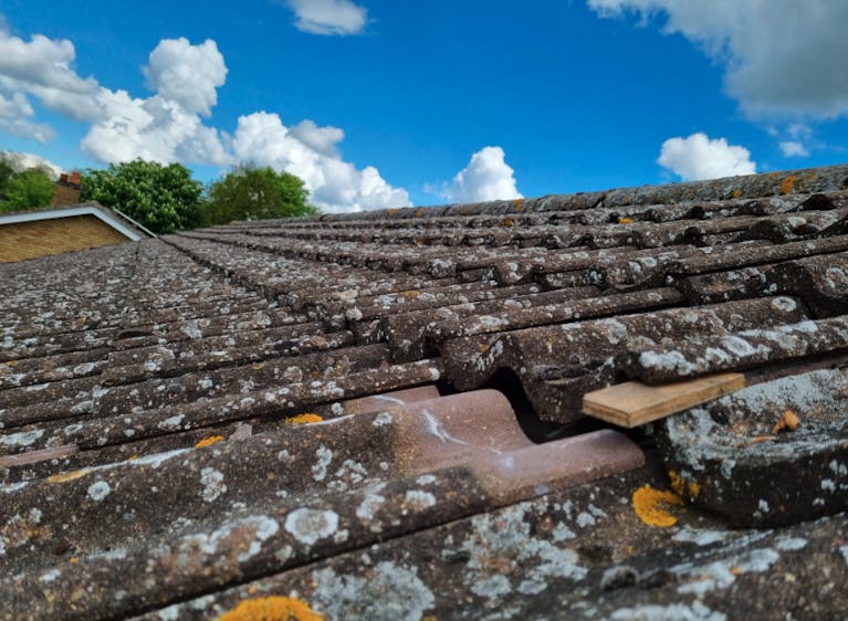 A loose tile among many other weather-worn tiles, against a blue sky with clouds