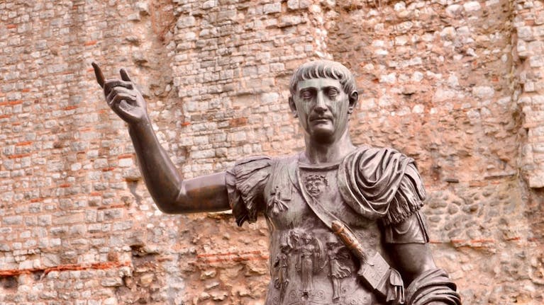 A bronze statue of a Roman emperor. In the background is a stone wall