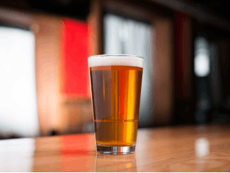Photo of a pint of beer standing on a wooden bar or table.