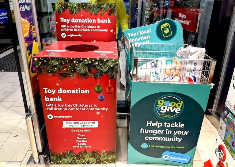 A red toy donation box and a green food donation box stand side by side in a supermarket