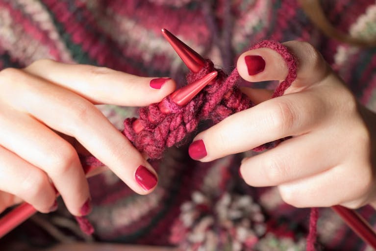 Caucasian hands with pink nails hold pink knitting and pink needles
