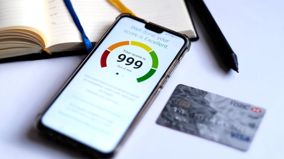 Mobile phone with a '999' credit score on its screen, plus a credit card and pen and notepad