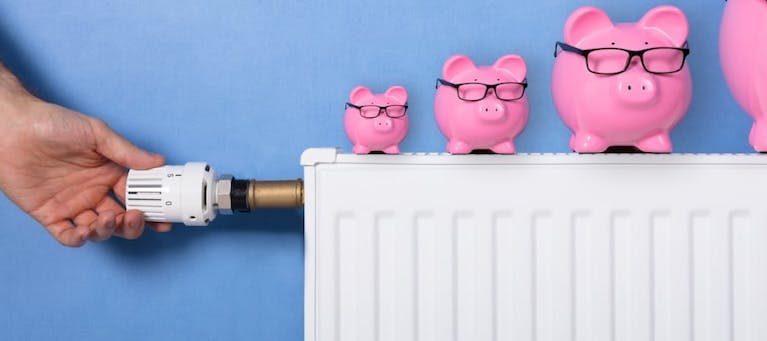 Piggy banks on a white radiator, a hand visible turning the knob at the left end