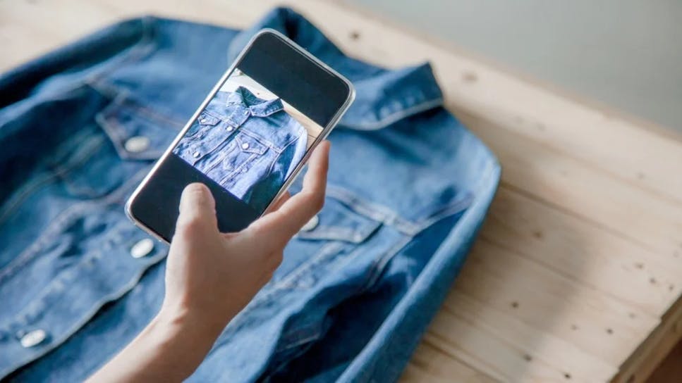 A person using their phone to take a photo of a jacket to sell online.